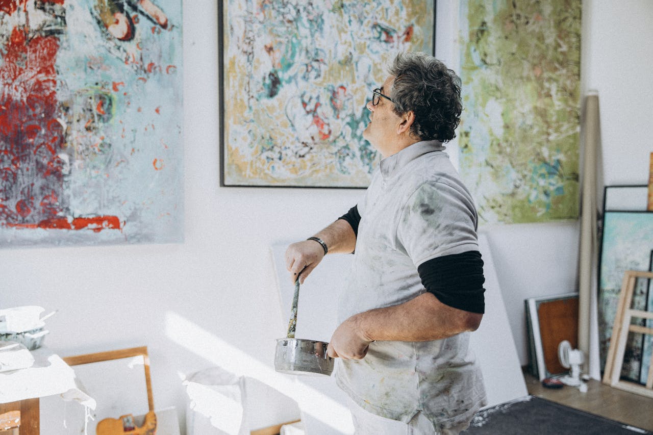 An artist painting on a canvas in a studio, surrounded by abstract artwork.