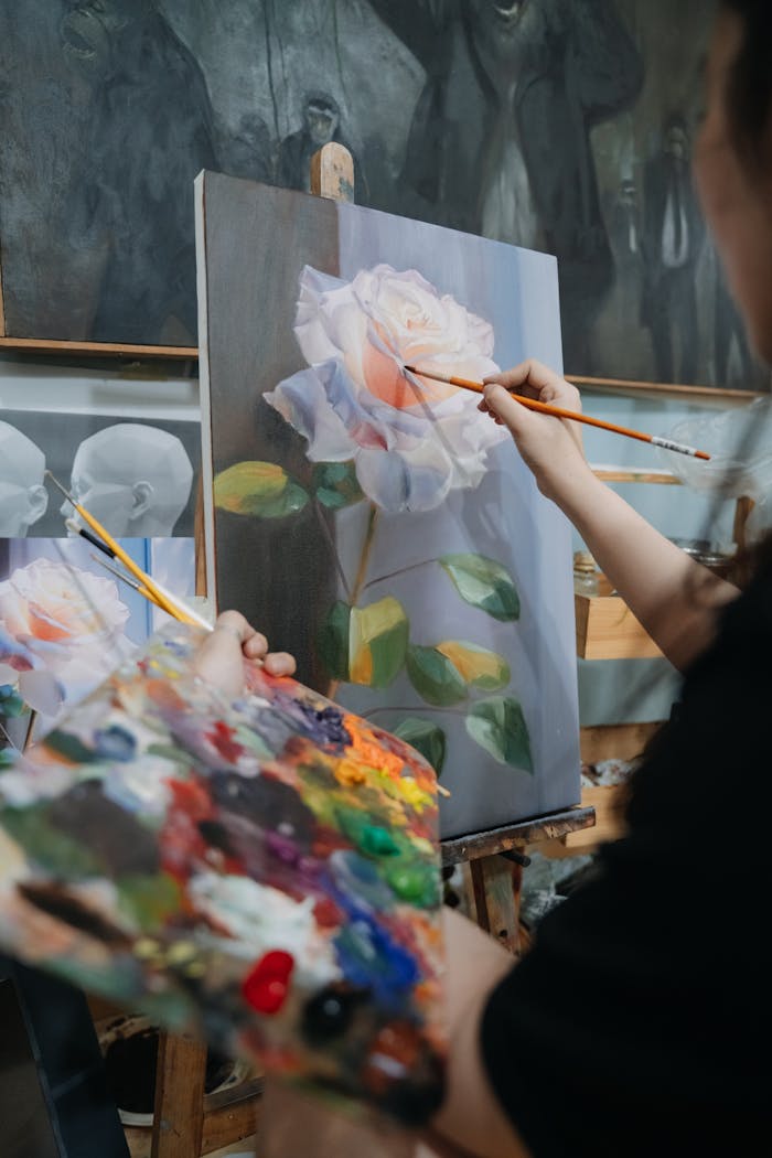 Artist painting a realistic rose on canvas using oil paints, showcasing vibrant colors and detailed brush techniques.